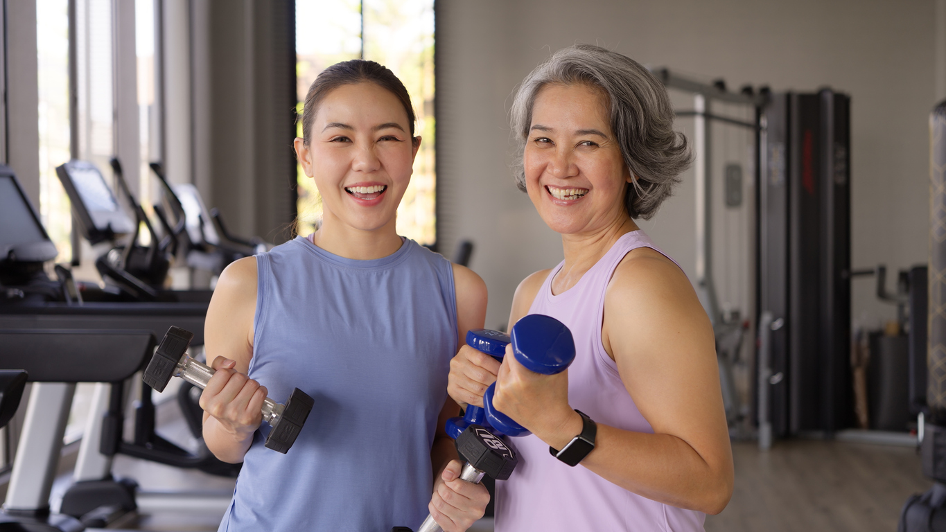 Young adult and middle age old mum smile look at camera strength training gym workout body weight picking up arm lift dumbbell. Elder people happy healthy aging life sport build muscle.